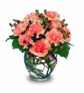 Orange carnations in a bouquet vase with berries and leather leaf